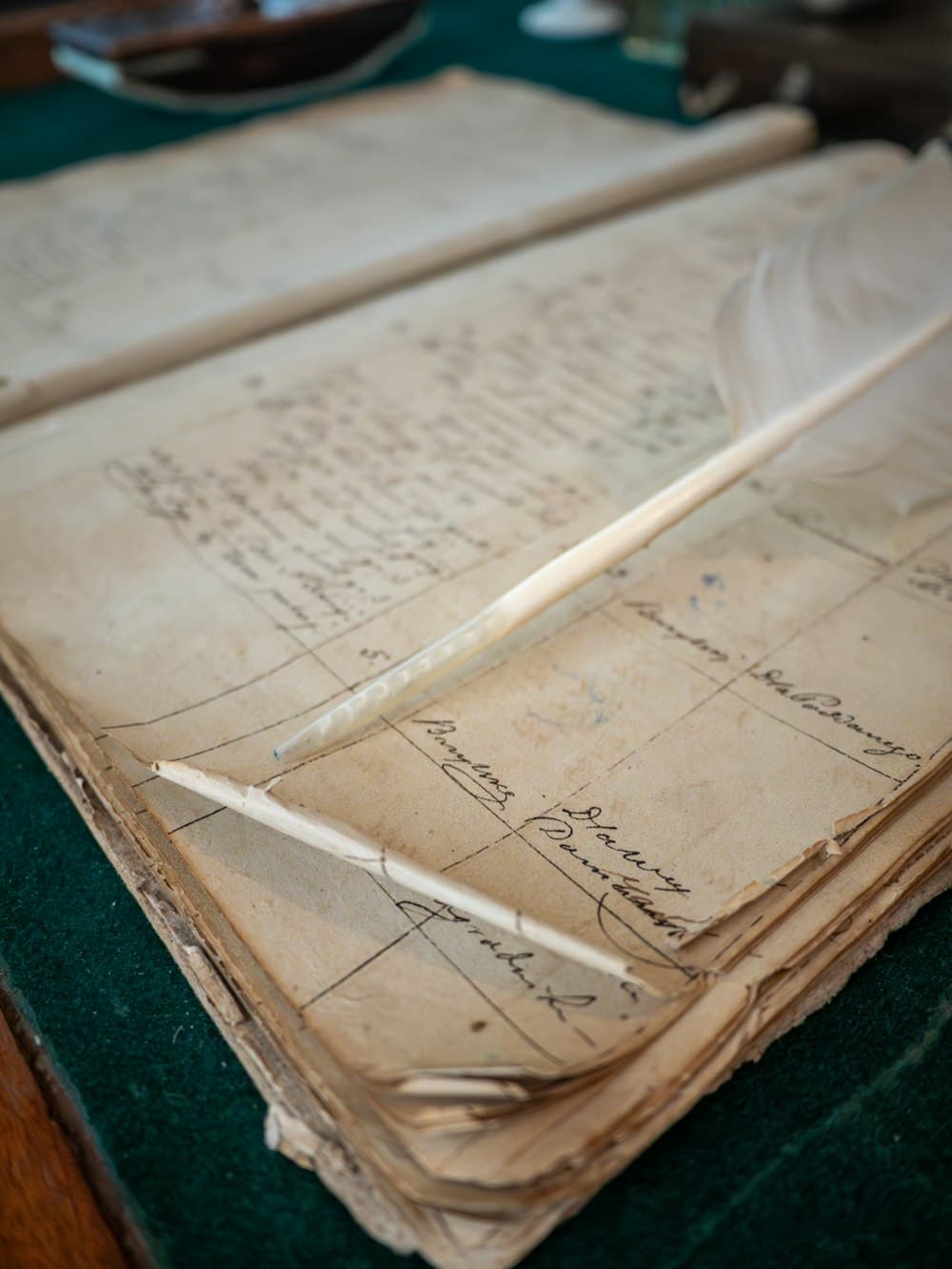 A feather quill resting on an old handwritten ledger