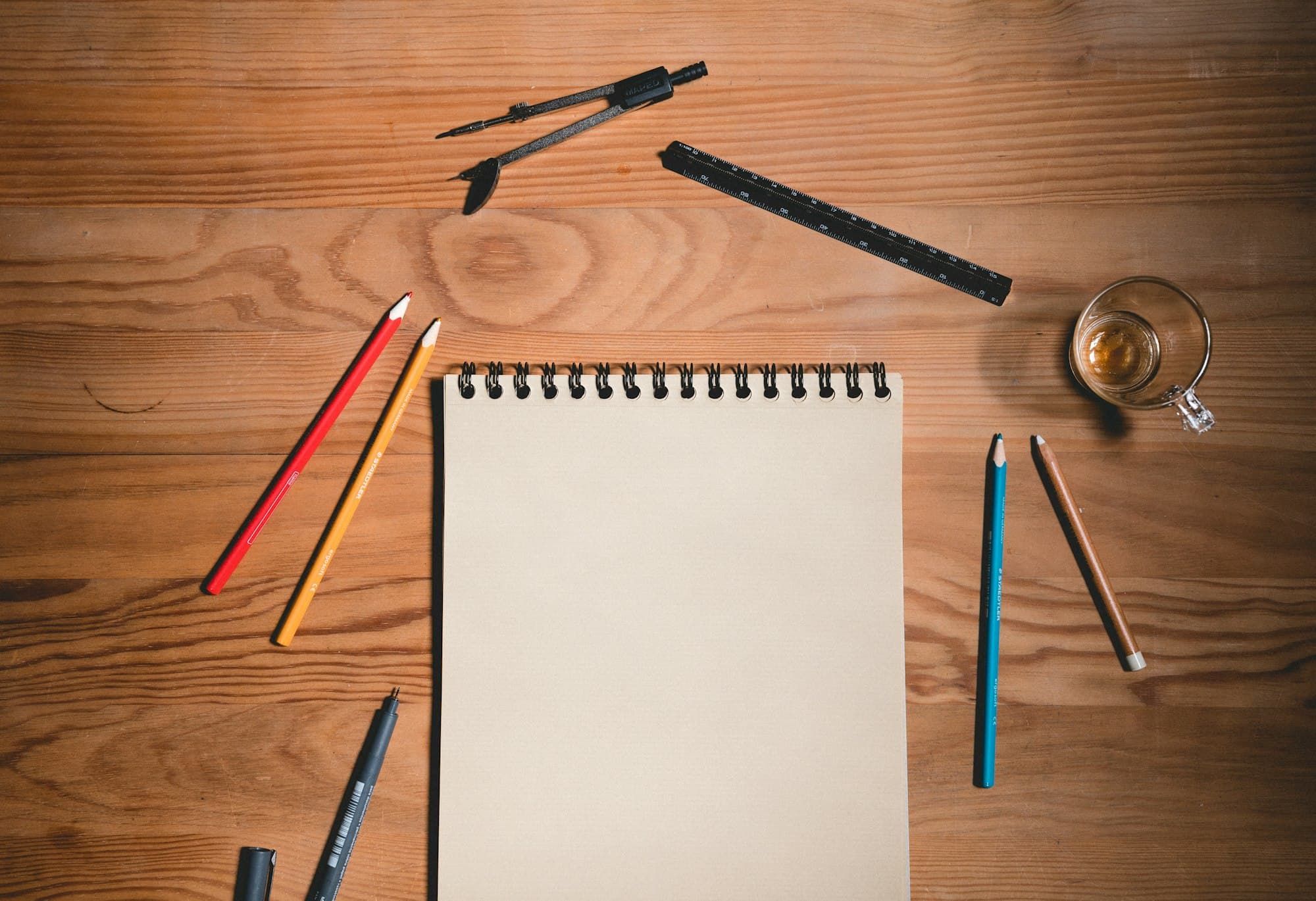 A wooden desk with a sheet of paper and drawing tools laid out
